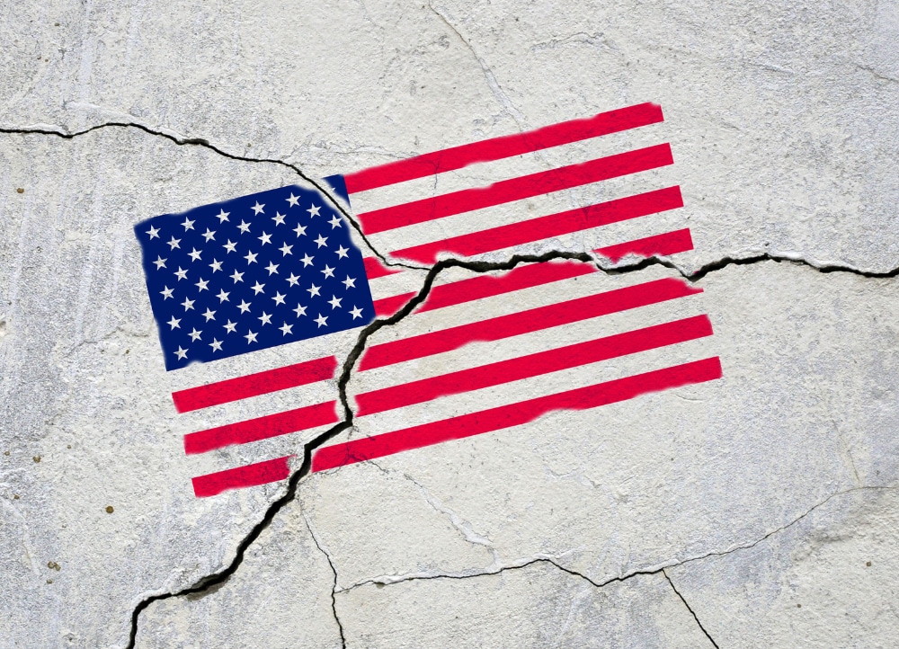 Photograph of an American flag painted onto a sidewalk that has cracked, fracturing the flag.