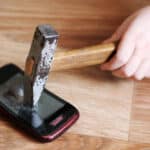 Photo of a child's hand smashing a hammer into a smartphone.