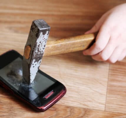 Photo of a child's hand smashing a hammer into a smartphone.