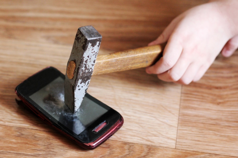 Photo of a child's hand smashing a hammer into a smartphone.