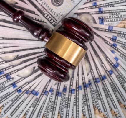 Photograph of a judge's gavel resting on top of a wheel of one hundred dollar bills.