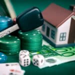 Photograph of a gambling problem, including playing cards, poker chips, and dice, and a care key and toy house representing losses.