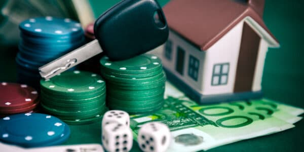 Photograph of a gambling problem, including playing cards, poker chips, and dice, and a care key and toy house representing losses.