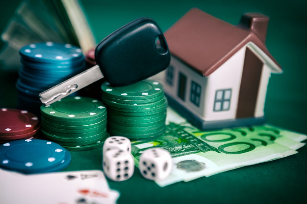 Photograph of a gambling problem, including playing cards, poker chips, and dice, and a care key and toy house representing losses.