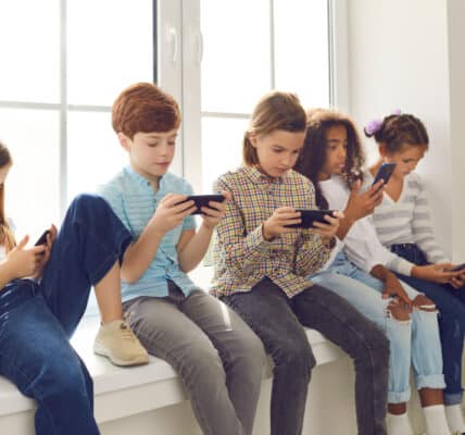 Photograph of a group of five children sitting in a window well each looking at their smartphones.