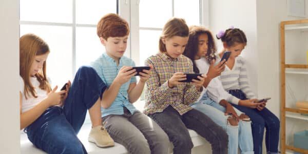 Photograph of a group of five children sitting in a window well each looking at their smartphones.
