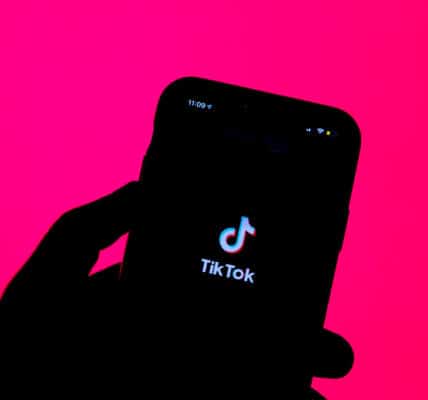Backlit photo of a hand holding a smartphone with the TikTok logo illuminated.