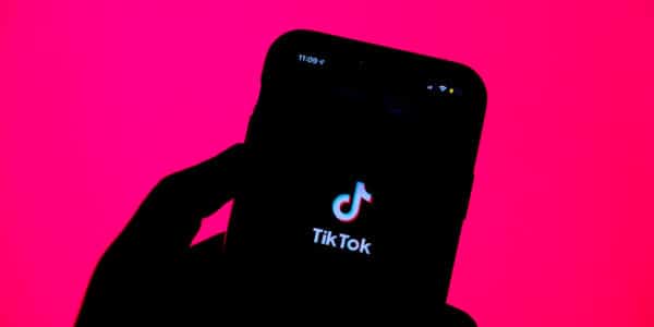 Backlit photo of a hand holding a smartphone with the TikTok logo illuminated.