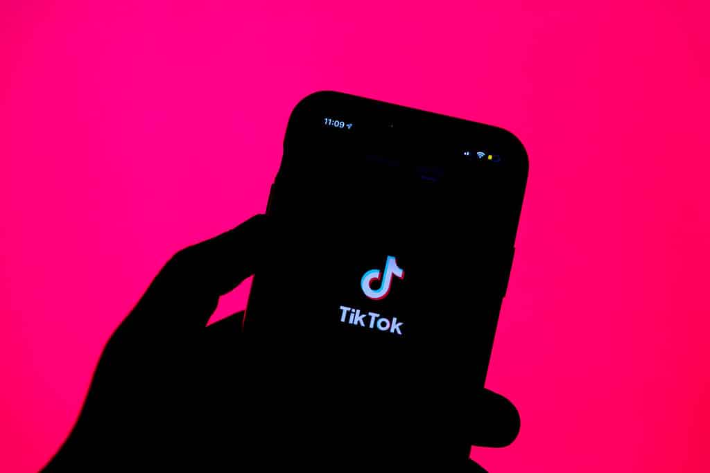 Backlit photo of a hand holding a smartphone with the TikTok logo illuminated.