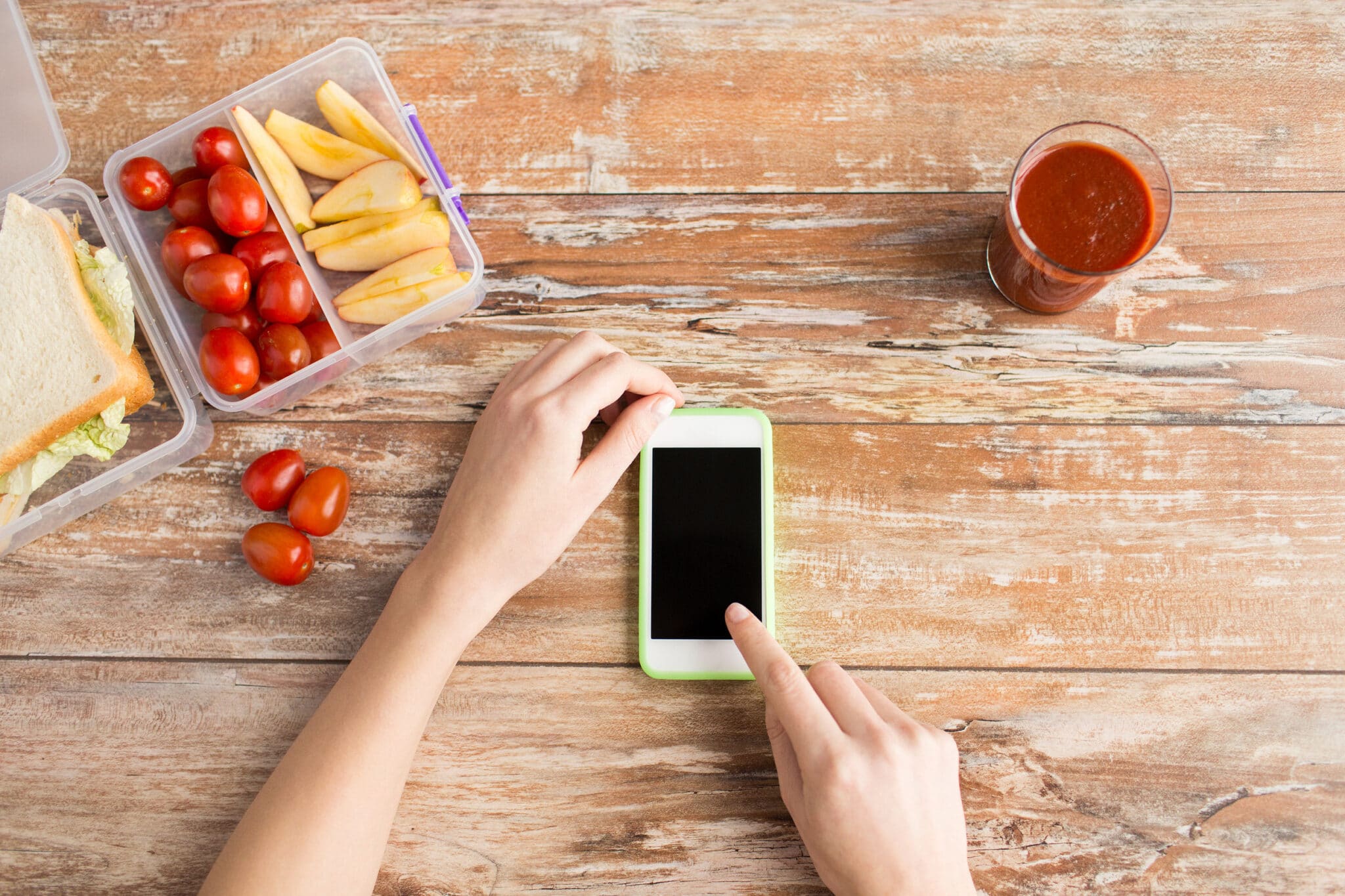 healthy eating, dieting, technology and people concept - close up of woman hands with blank smartphone and food in plastic container on table at home