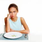 Portrait of very thin girl looking at the camera with almost nothing on the plate in front of her.