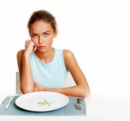 Portrait of very thin girl looking at the camera with almost nothing on the plate in front of her.