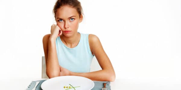 Portrait of very thin girl looking at the camera with almost nothing on the plate in front of her.