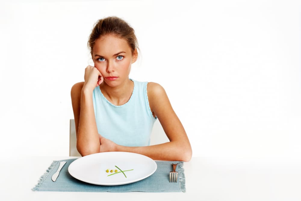 Portrait of very thin girl looking at the camera with almost nothing on the plate in front of her.