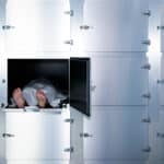 Staged photograph of a body covered with a white sheet on a morgue table in a locker.