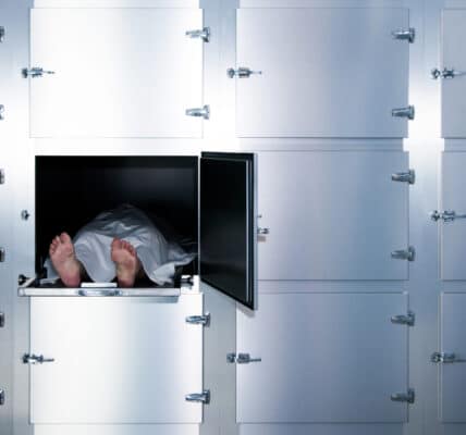 Staged photograph of a body covered with a white sheet on a morgue table in a locker.