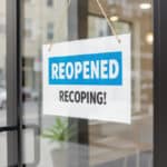 Photo of a small business recovery sign on glass door with reopened message