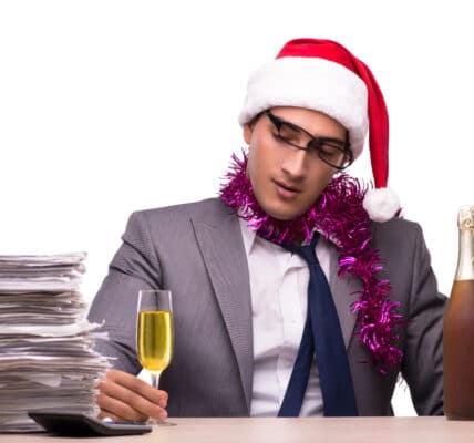 Photo of young businessman celebrating the holidays in his office with a flute of champagne.