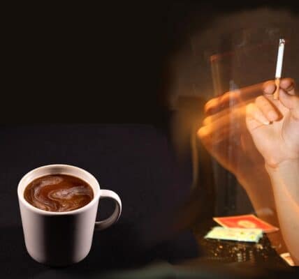 A hand holding a lit cigarette, and a cup of coffee on the table.