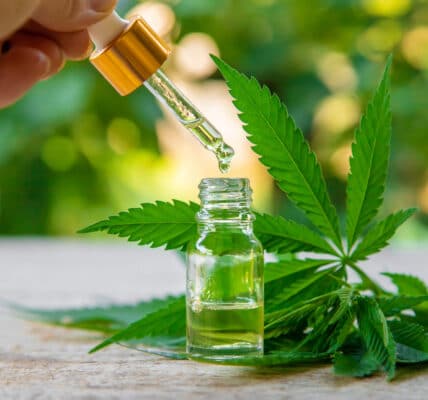 Photograph of an extract from marijuana plant containing a THC-based, non-opioid pain killer in a vial next to several leaves.