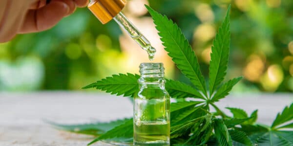 Photograph of an extract from marijuana plant containing a THC-based, non-opioid pain killer in a vial next to several leaves.