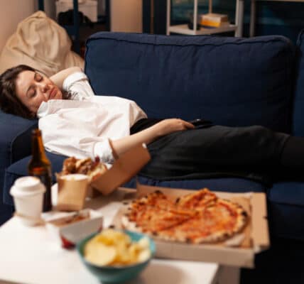 Photograph of woman falling asleep after eating junk-food in living room late at night.