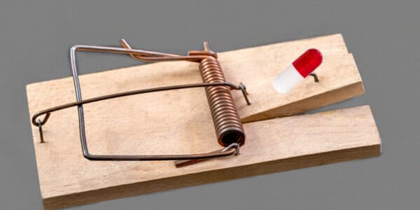 Photo of a mouse trap with a medicinal capsule on a grey background