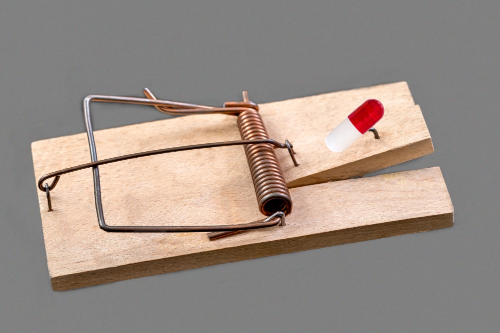 Photo of a mouse trap with a medicinal capsule on a grey background