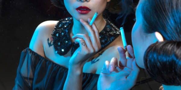 A photograph of a dressed-up woman holding a cigarette and looking in the mirror.