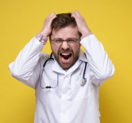 Photo of young doctor, stressed or furious, pulls his hair out and screams. Yellow background.