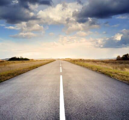 An image of an empty road with a vast landscape and the sky.