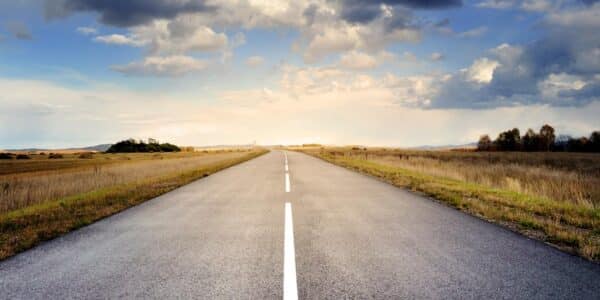 An image of an empty road with a vast landscape and the sky.