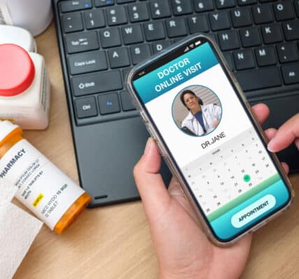 Photo of a telehealth session including smartphone, computer keyboard, and prescription bottles.