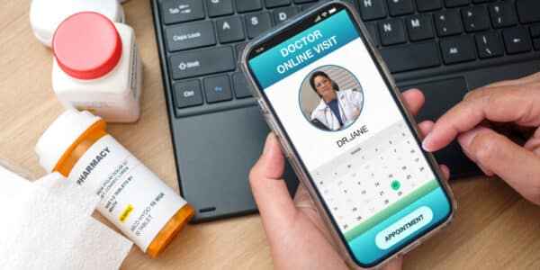 Photo of a telehealth session including smartphone, computer keyboard, and prescription bottles.