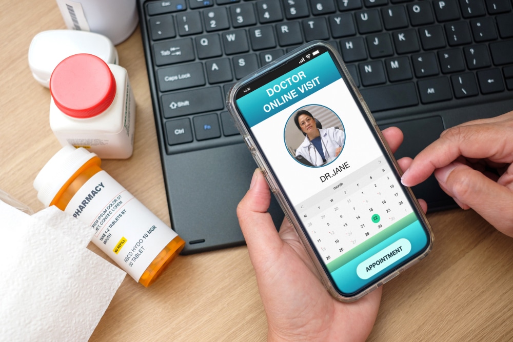 Photo of a telehealth session including smartphone, computer keyboard, and prescription bottles.