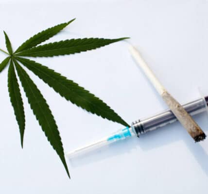 Photo of a marijuana leaf and a cannabis cigarette laying on top of an empty syringe.