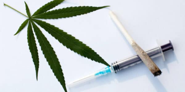 Photo of a marijuana leaf and a cannabis cigarette laying on top of an empty syringe.