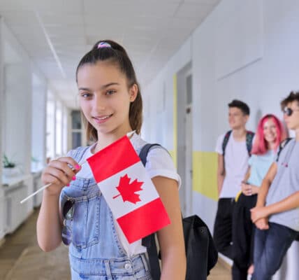 Photo of a teenage female student with flag of Canada inside school hallway with other teens in background.