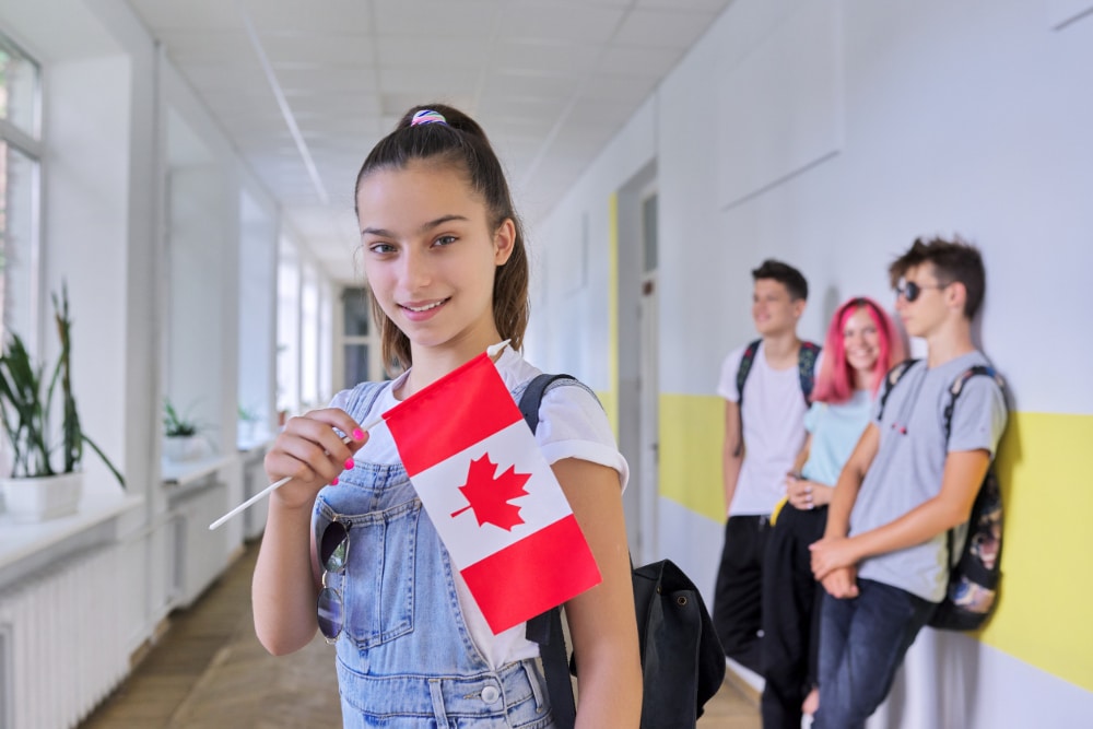 Photo of a teenage female student with flag of Canada inside school hallway with other teens in background.