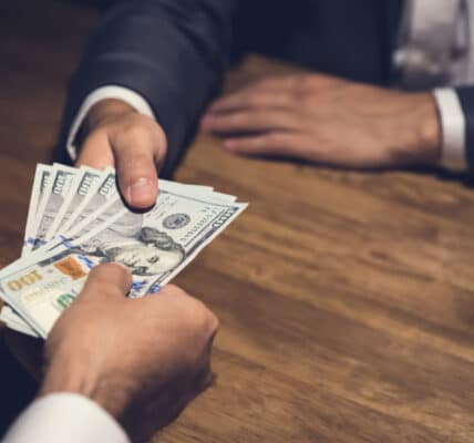 Photo of businessman giving money, US dollar (USD) bills, to nonprofit manager - bribery, corruption concept.