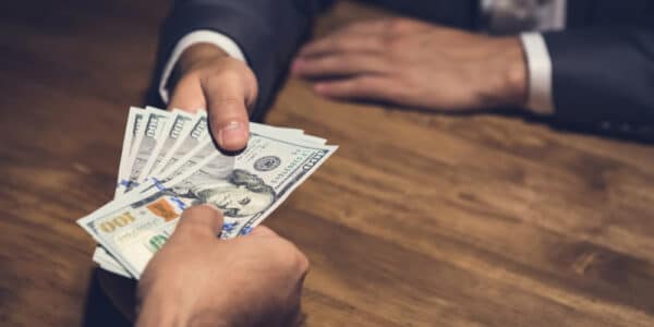 Photo of businessman giving money, US dollar (USD) bills, to nonprofit manager - bribery, corruption concept.