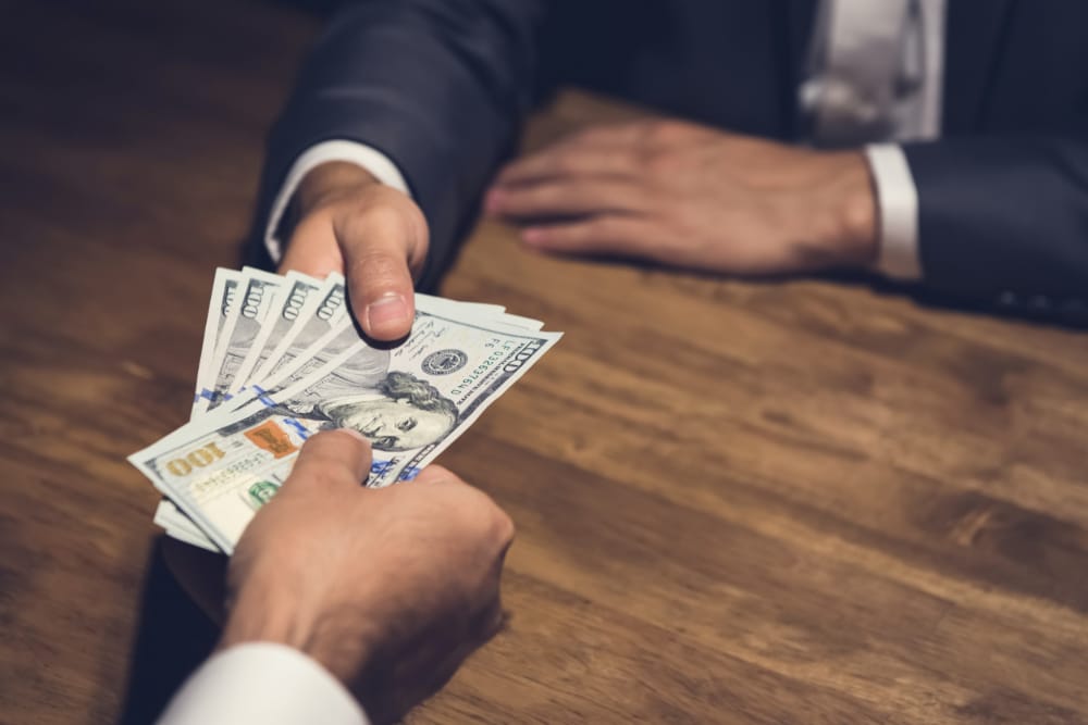 Photo of businessman giving money, US dollar (USD) bills, to nonprofit manager - bribery, corruption concept.