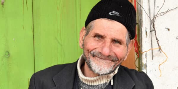 Photograph of a weathered old man with a pleasant smile against a weathered background.