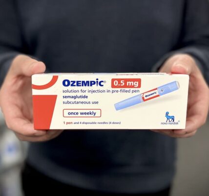 Photograph of a pharmacist holding a box of Ozempic injection pens.