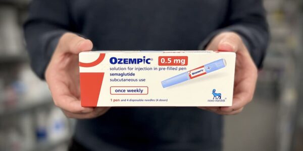 Photograph of a pharmacist holding a box of Ozempic injection pens.