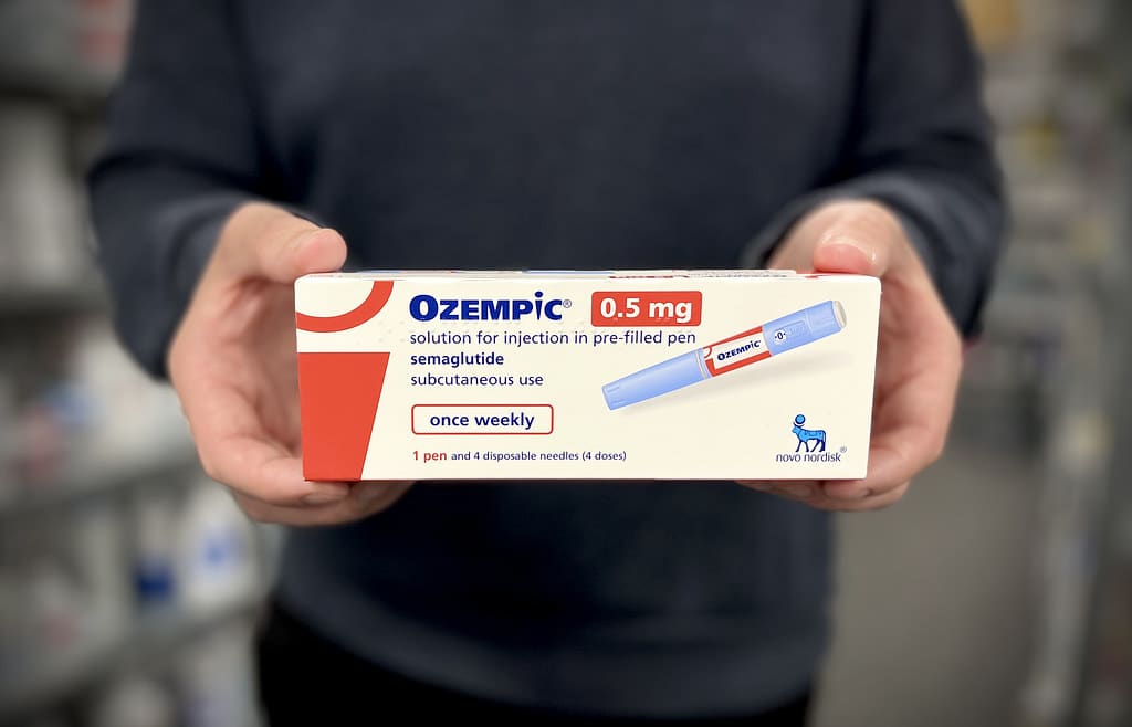 Photograph of a pharmacist holding a box of Ozempic injection pens.