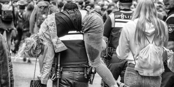 A black-and-white photo of a police officer in Amsterdam carrying a drunk young woman in a crowd.