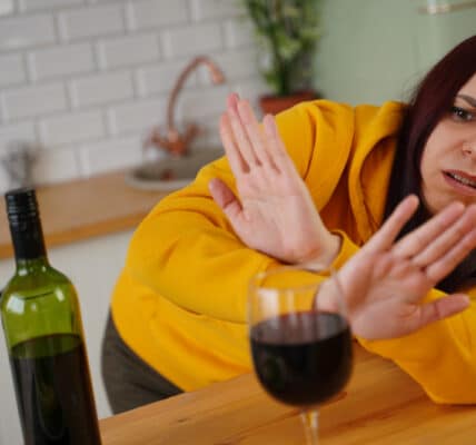 Photo of a woman in a kitchen rejecting a glass of wine.