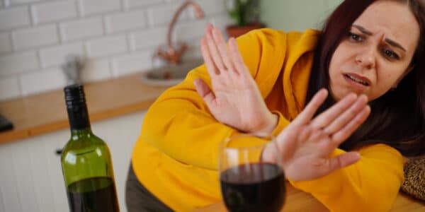 Photo of a woman in a kitchen rejecting a glass of wine.