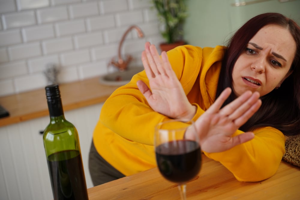 Photo of a woman in a kitchen rejecting a glass of wine.